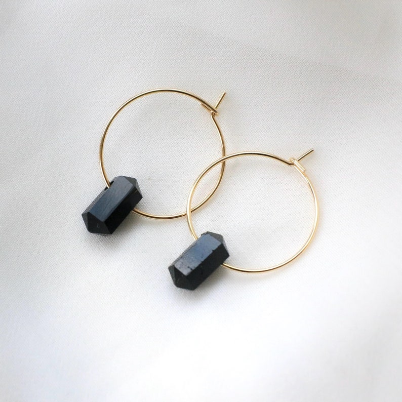 May include: A pair of gold hoop earrings with black gemstone accents. The earrings are simple and elegant, perfect for everyday wear.