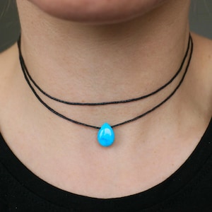 Peut inclure: Un collier ras de cou délicat avec un pendentif en forme de larme turquoise suspendu à un cordon noir. Le collier est composé de deux cordons.