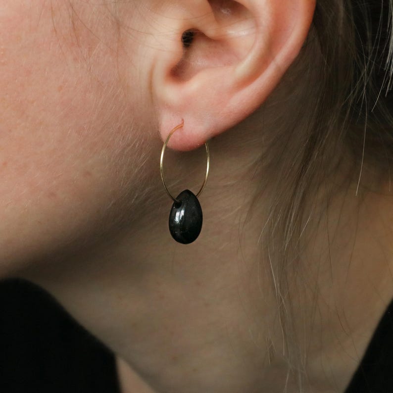 May include: Gold hoop earrings with a black gemstone dangle. The earrings are simple and elegant.