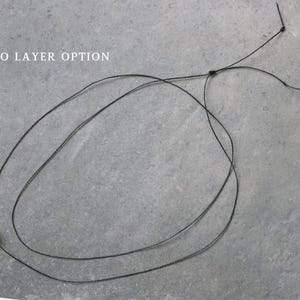 May include: A black necklace with a two-layer design. The necklace features a small, dark-colored bead and is displayed against a gray background. The text "TWO LAYER OPTION" is visible in the image.