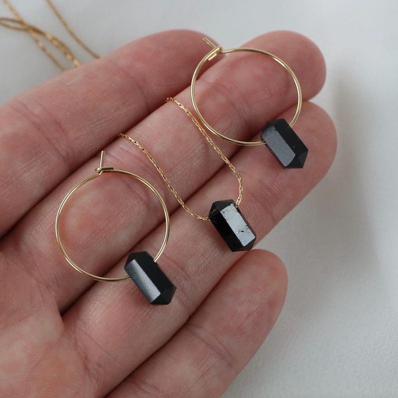 May include: A set of gold hoop earrings and a necklace with black gemstone pendants. The earrings and necklace feature a simple, minimalist design.