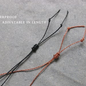 May include: Close-up of two adjustable cords, one black and one brown, with knots. The text "WATERPROOF EASY ADJUSTABLE IN LENGTH" is in white letters at the top. The cords are on a grey surface.