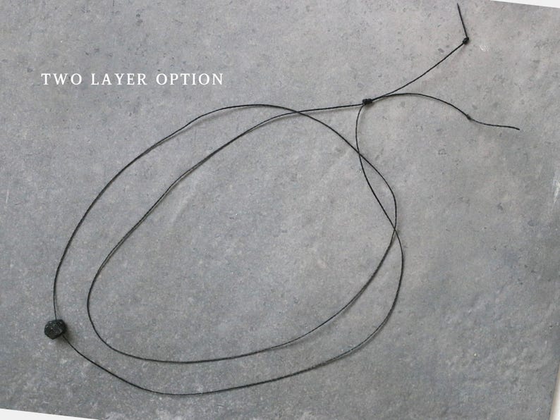 May include: A black necklace with a two-layer design. The necklace has a small, dark-coloured bead and is shown against a grey background. The text "TWO LAYER OPTION" is visible in the image.