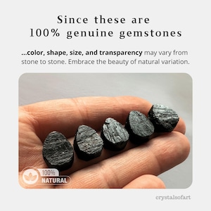 May include: Five black gemstones are held in a hand. The gemstones are teardrop-shaped and have a rough texture. The image includes the text "Since these are 100% genuine gemstones" and "100% NATURAL".