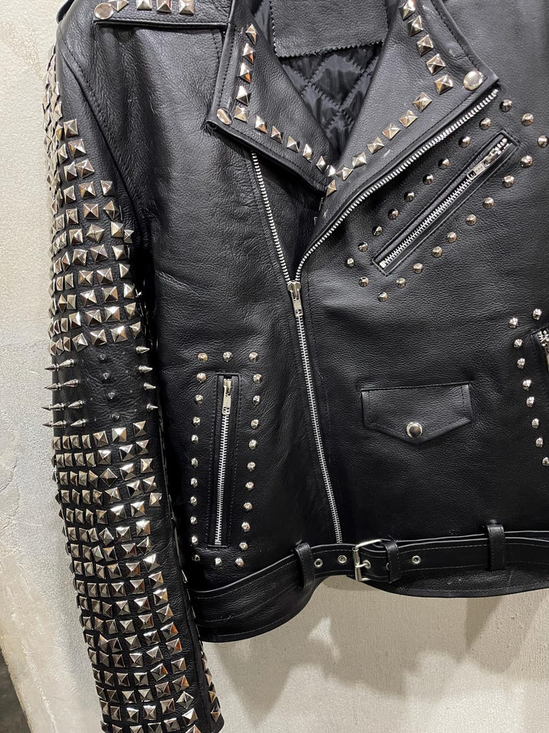 Puede incluir: Una chaqueta de cuero negra para motocicleta con tachuelas piramidales de metal plateado que cubren toda la manga y las solapas. La chaqueta incluye una cremallera frontal diagonal, varios bolsillos con cremallera, un bolsillo peque&ntilde;o con solapa y un cintur&oacute;n.
