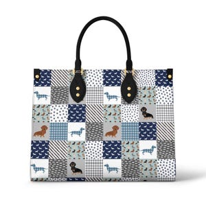 Puede incluir: Un bolso tote de cuero negro con un diseño de patchwork que presenta un patrón de cuadrados azules, blancos y grises. Cada cuadrado tiene una pequeña silueta de dachshund en varios colores.