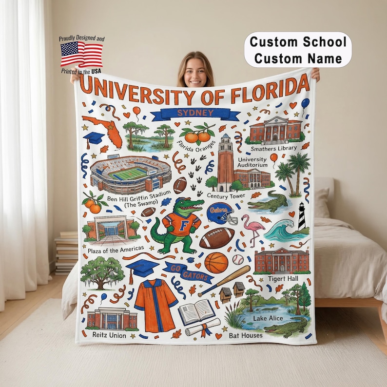 May include: A white University of Florida blanket featuring a colorful illustrated design with the text "UNIVERSITY OF FLORIDA" and "SYDNEY". The design includes landmarks, a gator mascot, and the words "GO GATORS".