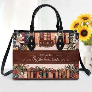 Può includere: Borsa rettangolare con manici neri e tracolla. La borsa presenta un design floreale e di libri con il testo "MARTHA" e "JUST A GIRL Who loves books". La borsa ha una fascia marrone simile alla pelle al centro.