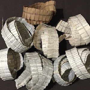 May include: A collection of vintage paper rolls, some with text and some with stitching, are arranged on a dark surface. The text on the rolls includes words like "Drawing Board", "T-Squares", and "Florence".