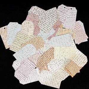 May include: A pile of vintage-style paper tags with handwritten text in various shades of brown, pink, and blue. The tags are all different shapes and sizes, and some have holes punched in them.