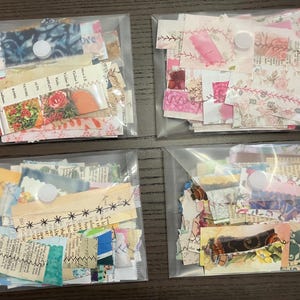 May include: Four clear plastic pouches filled with assorted fabric scraps. The scraps feature floral, patterned, and text designs in various colors. Each pouch is sealed with a white snap closure. Ideal for crafting and scrapbooking.