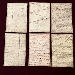 May include: Six handmade paper envelopes with handwritten script. The envelopes are various sizes and shapes, with a vintage aesthetic. The paper has a distressed, aged appearance, with visible stitching along the edges. The script is in a faded, sepia tone.