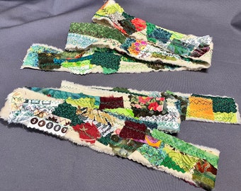 May include: Two strips of fabric made from scraps of different fabrics sewn together. The fabric scraps are in various colors, including green, red, yellow, and brown. The fabric strips are sewn together with a white fabric backing.
