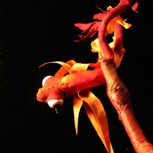 May include: A red and orange fabric dragon with a white eye, perched on a branch.