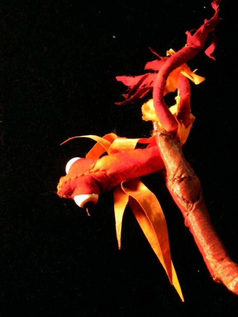 May include: A red and orange fabric dragon with a white eye, perched on a branch.