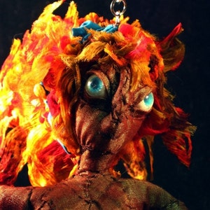 May include: A handmade doll with a brown fabric body, orange and red hair, and blue eyes. The doll is wearing a blue fabric headband and has a stitched-on mouth.