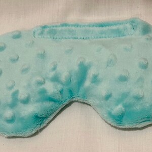 May include: A light blue sleep mask with a textured, dotted surface. The mask has a curved shape to fit around the eyes and a band across the top. The soft material is likely for comfort.