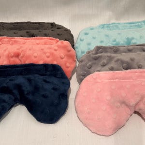 May include: An assortment of six eye masks in various colors. The masks are made of a soft, textured fabric and come in shades of navy blue, coral, pink, gray, teal, and brown. The eye masks are designed to block out light.