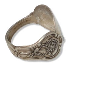 May include: Silver spoon ring with a floral design. The spoon is bent into a ring shape and has a clover design on the front. The back of the ring is marked "1847 Rogers Bros."