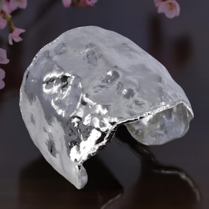 May include: A silver cuff bracelet with a hammered, textured finish. The bracelet is open and has a slightly irregular shape.