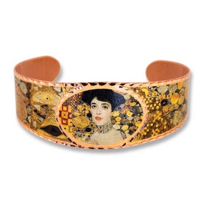 May include: Copper bracelet with a gold-toned oval design featuring a portrait of a woman with dark hair and a floral background. The bracelet has a textured edge.
