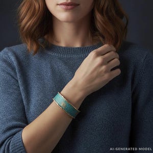 A close-up of a woman wearing a blue sweater and a turquoise bracelet, with her hand resting on her chin.