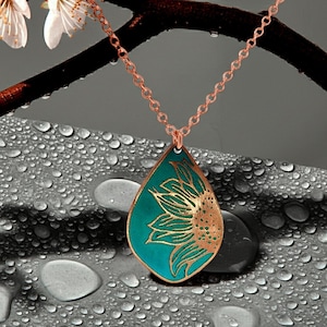 May include: A teardrop-shaped pendant necklace featuring a copper-colored sunflower design etched onto a vibrant teal background. The pendant hangs from a delicate copper-toned metal chain, showcasing a detailed floral motif with metallic edges.