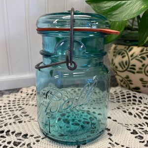 May include: A vintage blue glass Ball Ideal jar with a wire bail closure and a red rubber lid.