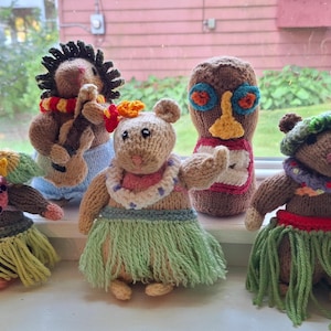 May include: Seven knitted animal figurines wearing colorful hula skirts. The figurines are a brown and white hedgehog, a brown and white mouse, a brown and white rabbit, a brown and white squirrel, a brown and white bear, a brown and white monkey, and a brown and white cat.