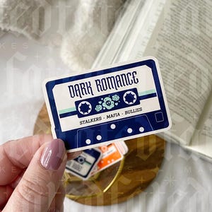 Pu&ograve; includere: Un adesivo a forma di cassetta blu e bianca con il testo "Dark Romance" e "Stalkers - Mafia - Bullies" stampato su di esso.