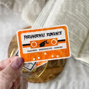 Pu&ograve; includere: Sticker a forma di cassetta arancione e nero con il testo "Paranormal Romance" e "Vampires - Werewolves - Demons".