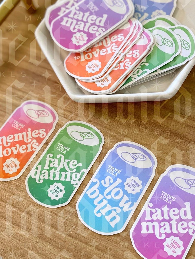 May include: Four colorful stickers shaped like soda cans with different phrases on them. The phrases are "Fated Mates", "Fake Dating", "Slow Burn", and "Enemies Lovers". Each sticker has a white circle with the text "I Drink That Shit Up" in black.