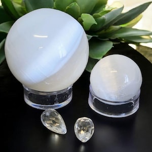 May include: Two white selenite spheres on clear stands, with two smaller clear selenite points on a black surface.