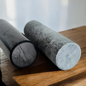 Puede incluir: Dos jarrones cilíndricos, uno negro y otro gris, hechos de un material texturizado. Los jarrones están sobre una superficie de madera.