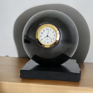 May include: A black sphere clock with a gold rimmed face and gold hands. The clock is sitting on a black square base.