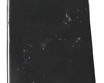 May include: A black rectangular slab of obsidian with a smooth, polished surface. The stone has a few small, white inclusions.
