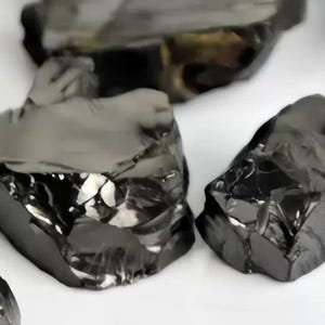 May include: A collection of black obsidian stones, each with a unique, rough, and jagged shape. The stones have a dark, glossy finish and are arranged on a white surface.