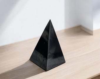 May include: A black obsidian pyramid on a light wood surface.