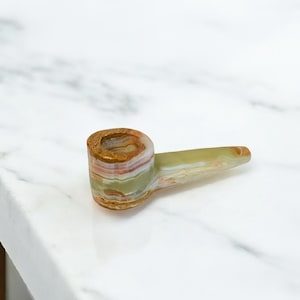 May include: A green and brown striped stone pipe with a rounded bowl and a long, thin stem.