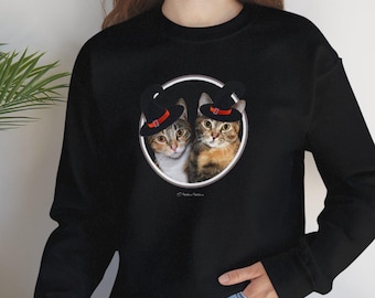 May include: Black sweatshirt featuring a circular graphic of two cats wearing hats. The cats have brown and grey fur. The hats are black with a red band. The sweatshirt is long-sleeved and made of a soft material.