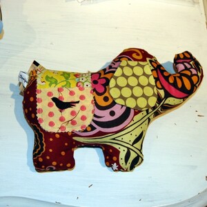 May include: A colorful patchwork elephant toy with a brown, yellow, green, pink, and orange design. The elephant has a small black bird on one of the patches.