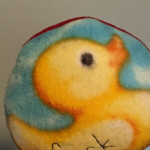 May include: A felt ball with a blue and white cloud pattern and a yellow duck with a black eye. The duck is facing to the right.