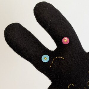 May include: Black felt bunny with yellow stitching and three buttons: one blue, one pink, and one yellow.