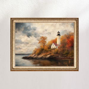 Puede incluir: Pintura paisajística enmarcada de un faro en una costa rocosa durante el otoño. El faro es blanco con la parte superior negra, sobre un fondo de colorido follaje otoñal. La pintura está en un marco dorado ornamentado.