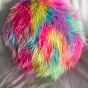 May include: A round, fluffy pillow with a rainbow pattern. The pillow is made of soft, colorful fur and is perfect for adding a touch of whimsy to any room.