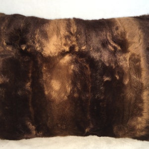 May include: A rectangular pillow with a brown fur texture. The pillow has a mix of dark and light brown tones, creating a natural, textured appearance. The fur appears soft and plush, suggesting a comfortable home decor item.