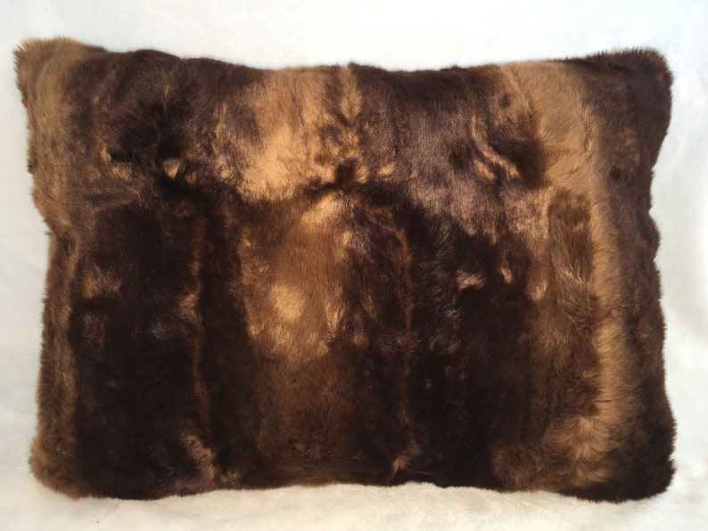 May include: A rectangular pillow with a brown fur texture. The pillow has a mix of dark and light brown tones, creating a natural, textured appearance. The fur appears soft and plush, suggesting a comfortable home decor item.