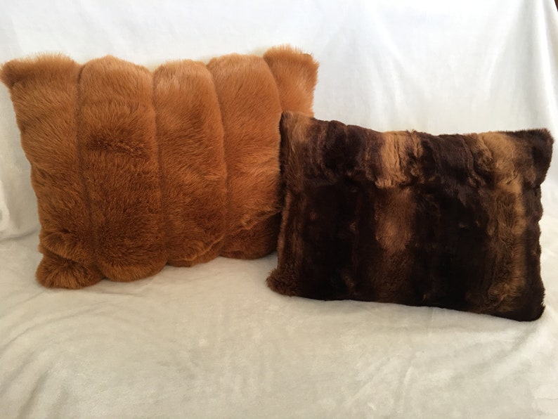 May include: Two decorative throw pillows. One is a light brown color with a ribbed design. The other pillow is a darker brown with a textured appearance. Both pillows have a soft, plush texture and are rectangular in shape.