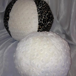 May include: Two plush balls. One ball is white with a textured surface and the other is white and black leopard print. The balls are made of a soft, textured fabric. The leopard print ball is divided into sections.