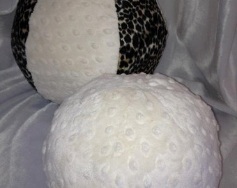 May include: Two plush balls. One ball is white with a textured surface and the other is white and black leopard print. The balls are made of a soft, textured fabric. The leopard print ball is divided into sections.